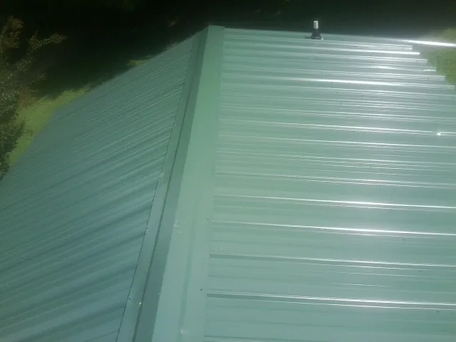 New green metal panels meeting at the ridge of a roof — Flat Roof Repair work by our crew in Wadsworth