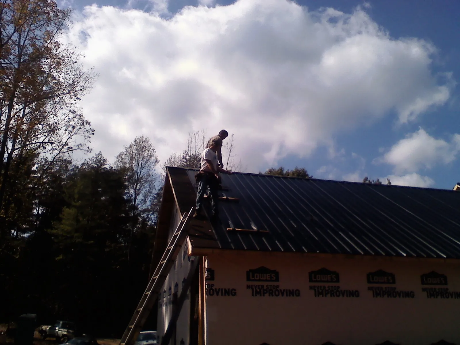 Roofer fastening dark metal panels high against a cloudy sky, from a Roof Inspection job in Wadsworth